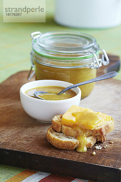 Honigsenf auf Brot mit Käse auf Holzbrett mit Glas und Löffel im Hintergrund