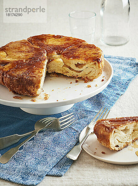 Kouign Amann auf einem Kuchenständer  ein Stück herausgenommen und auf einem Dessertteller mit Gabeln davor serviert