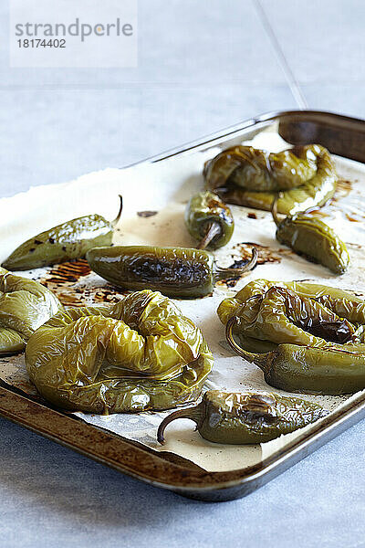 Geröstete grüne Paprika und Jalapenos auf einem mit Backpapier ausgelegten Backblech