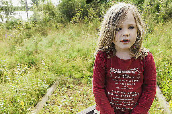 Nahaufnahme eines 3-jährigen Mädchens im roten Hemd  das auf einem Feld sitzt  Schweden