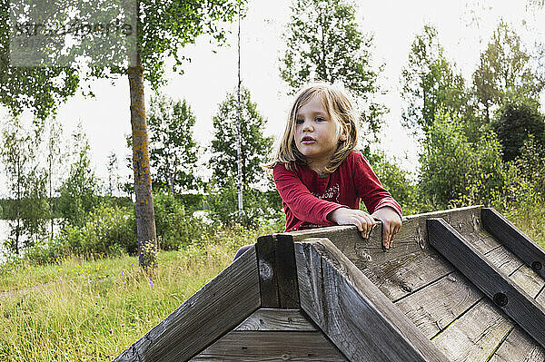 3 Jahre altes Mädchen im roten Hemd klettert auf einen Holzschuppen  Schweden