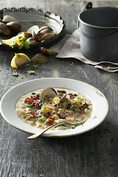 Schüssel mit Muschelsuppe auf einem grauen Holztisch mit Zutaten im Hintergrund