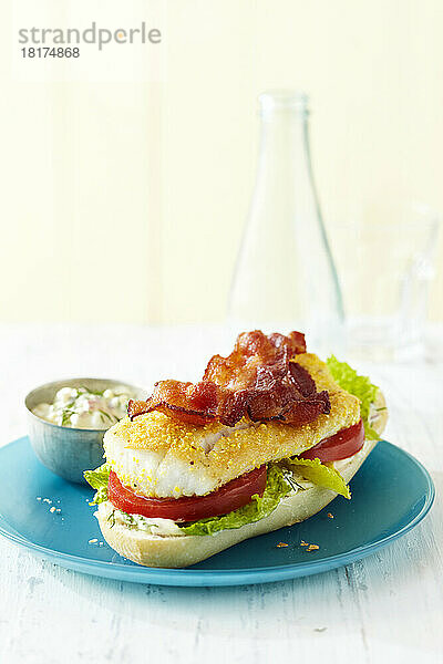 Offenes Fischsandwich mit Speck  Salat  Tomate und Mayonnaise auf einem blauen Teller