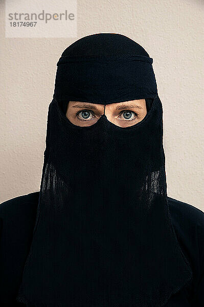 Close-up portrait of woman wearing black muslim hijab and muslim dress  looking at camera  studio shot on white background