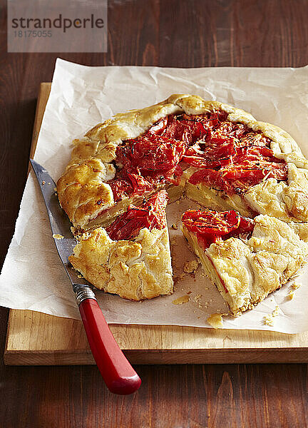 Tomato and potato galette on a cutting board with a knife and parchment paper