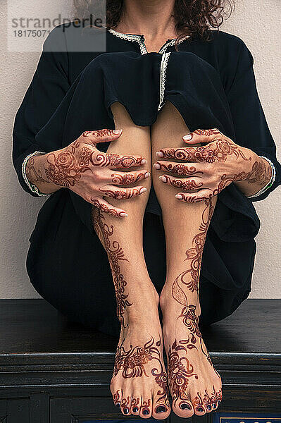 Unterer Teil einer Frau  die drinnen sitzt und Beine  Füße und Hände zeigt  die mit Henna im arabischen Stil bemalt sind  in einem typisch schwarzen  arabischen  muslimischen Kleid  Studioaufnahme