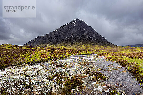 Fluss Etive und Bergkette Buachaille Etive Mor mit dunklem bewölktem Himmel bei Glen Coe in Schottland  Vereinigtes Königreich