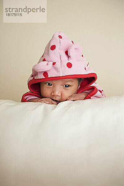 Portrait of two week old  newborn Asian baby girl in pink polka dot hooded jacket  studio shot on white background