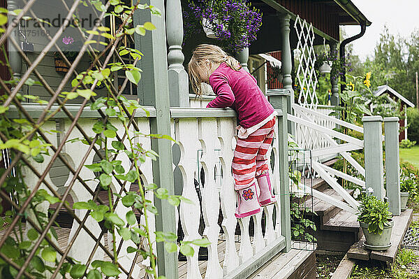 3 Jahre altes Mädchen in Gummistiefeln klettert auf Veranda  Schweden