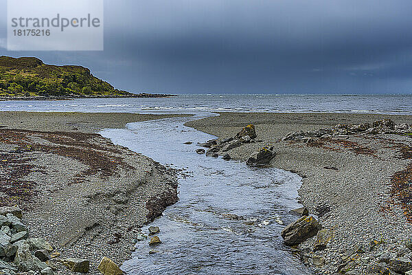 Fluss fließt in die Meeresbucht mit Gewitterwolken über dem Meer auf der Isle of Skye in Schottland  Vereinigtes Königreich