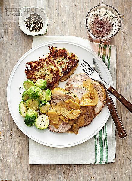Roast pork with apple sauce  brussels sprouts and potato patties on a white plate with fork and knife
