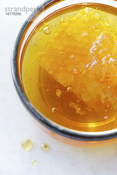 Nahaufnahme von oben auf klaren goldenen Honig in einem Glas mit Wabe und Luftblasen