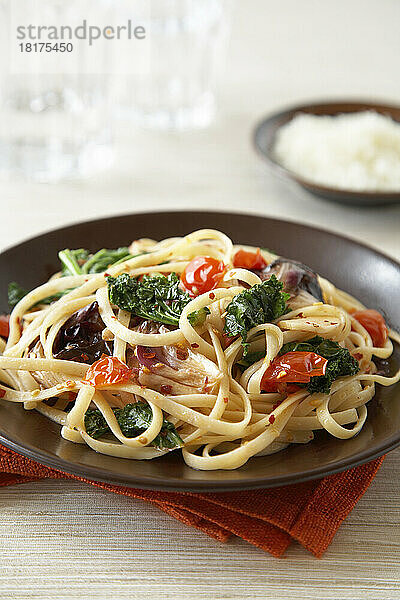 Linguine-Nudeln mit Tomaten  Blattgemüse und zerstoßener roter Paprika auf dunkelbraunem Teller