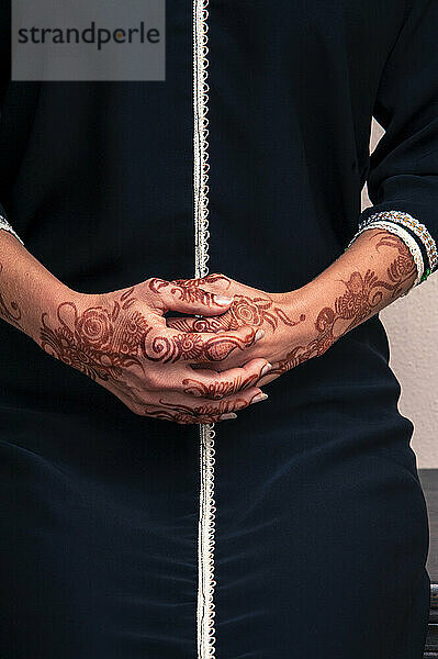 Frau sitzt drinnen mit Nahaufnahme gefalteter Hände  die mit Henna im arabischen Stil bemalt sind  trägt ein typisch schwarzes  arabisches  muslimisches Kleid  Studioaufnahme