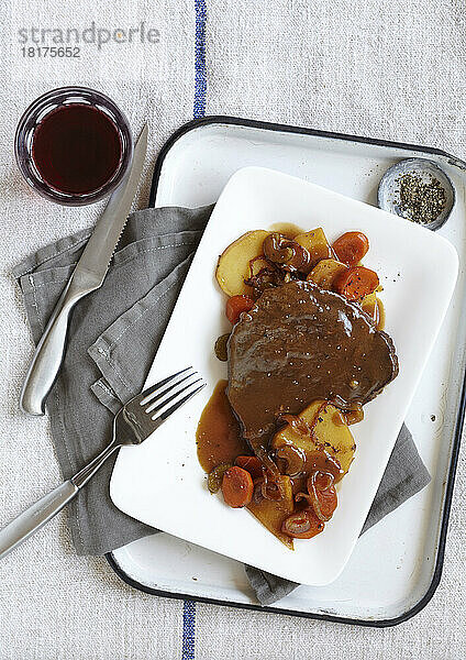 Steak mit Soße  serviert mit Kartoffeln  Karotten und Zwiebeln und einem Glas Rotwein