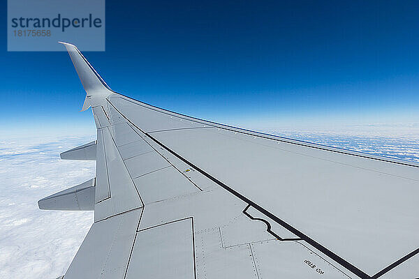 Blick auf den Flügel eines Flugzeugs im Flug über den Alpen