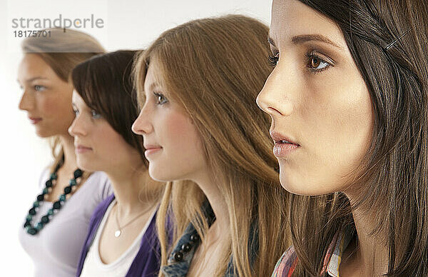 Nahaufnahmeporträt von vier jungen Frauen  die in einer Reihe stehen  Studioaufnahme auf weißem Hintergrund