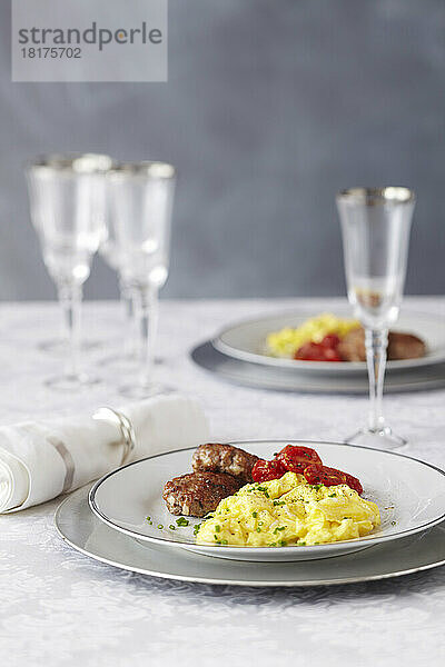 Brunch-Einstellung mit Rührei  Wurstpastetchen  gegrillten Tomaten und Champagnergläsern