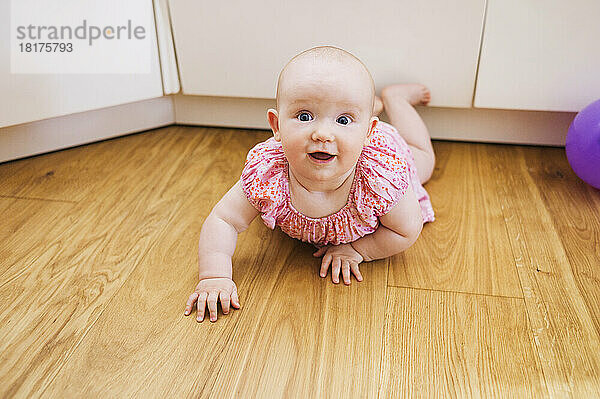 Porträt eines kleinen Mädchens  das auf dem Boden liegt und in die Kamera lächelt