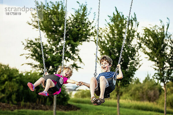 Junges Mädchen und Junge halten sich an den Händen  während sie auf einer Schaukel auf einem Spielplatz spielen; St. Albert  Alberta  Kanada