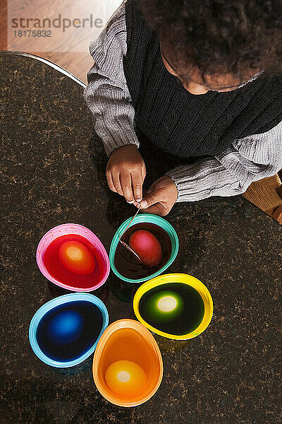 Overhead View of Boy using Coloring Cups to Dye Easter Eggs on Granite Kitchen Counter