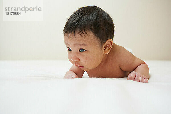 Newborn Asian baby with baby acne lying on stomach  studio shot on white background