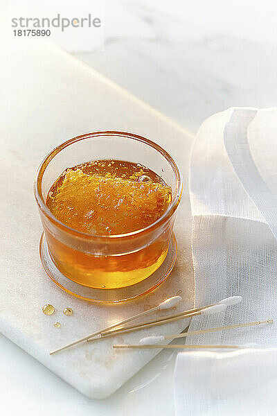 Ein kleines Glasgefäß mit klarem  goldenem Honig und eine Honigwabe mit Wattestäbchen. Hohes Schlüsselimage von Honig und Schönheitsprodukten.