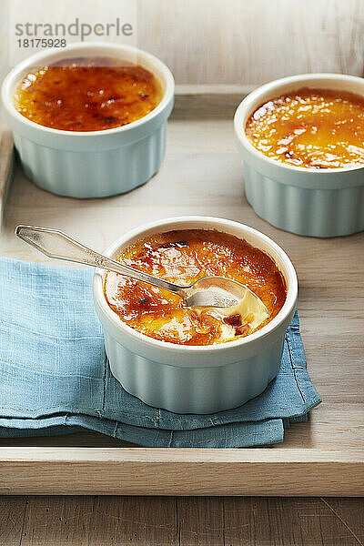 Drei Auflaufförmchen mit Crème Brûlée auf einem Holztablett