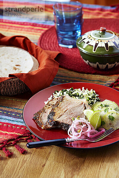 Mexikanisches Feiertagsfest mit Schweinefleisch und Reismehl auf einem roten Teller mit Tortillas als Beilage