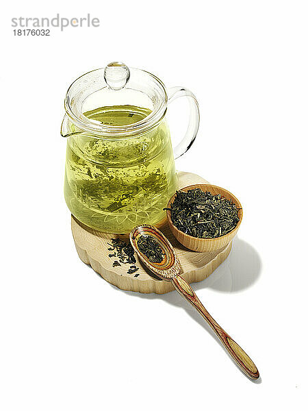 Grüner Tee in Teekanne mit getrockneten Teeblättern in Holzschale auf weißem Hintergrund ziehen lassen