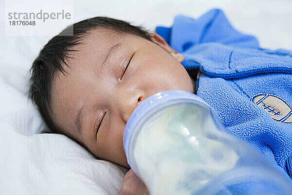 Close-up of two week old Asian baby girl sleeping while drinking from bottle  studio shot