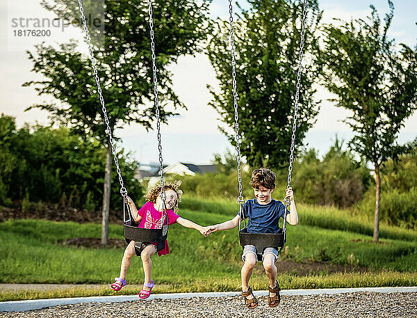 Junges Mädchen und Junge halten sich an den Händen  während sie auf einer Schaukel auf einem Spielplatz spielen; St. Albert  Alberta  Kanada
