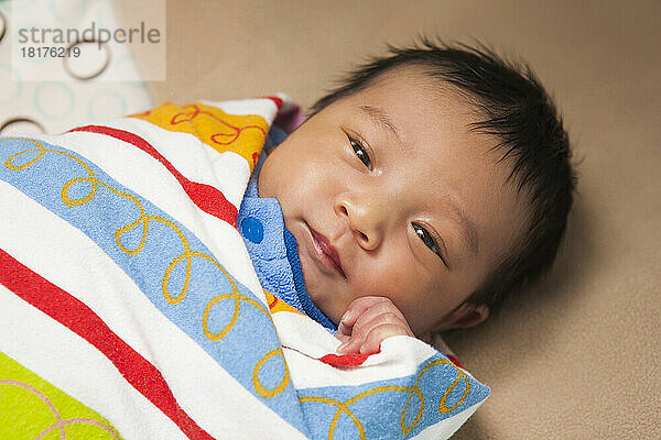 Close-up portrait of two week old  newborn Asian baby girl  wrapped in colorful swaddling blanket  studio shot