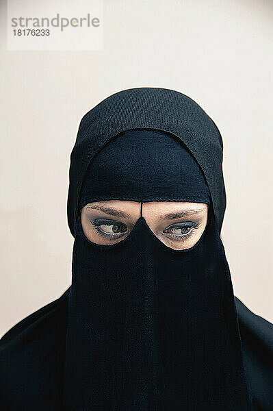 Nahaufnahme einer jungen Frau in schwarzem  muslimischem Hijab und muslimischer Kleidung  deren Augen zur Seite blicken und Augen-Make-up zeigen  Studioaufnahme auf weißem Hintergrund