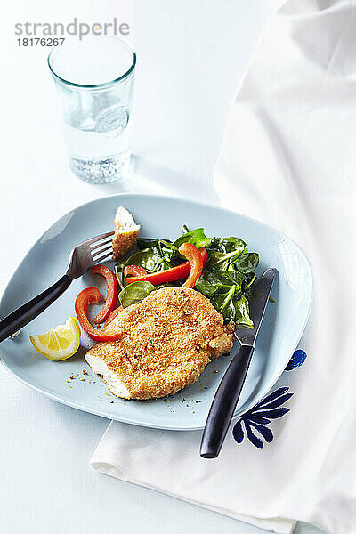 Hähnchenbrust mit Sesamkruste  Spinatsalat und roten Paprika auf einem blauen Teller