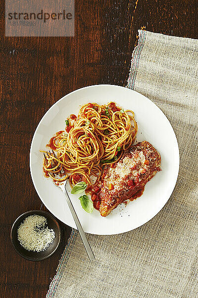 Teller mit Hühnerparmesan mit Spaghetti und Tomatensauce und einer Beilage mit einer Gabel und einer Beilage Käse auf einem hölzernen Hintergrund