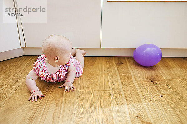 Kleines Mädchen liegt auf dem Boden und schaut auf den lila Ballon