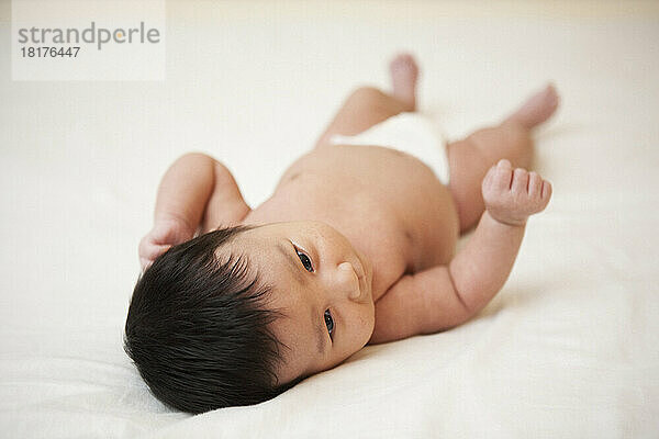 Newborn Asian baby in diaper lying on back  scratching head from baby acne  studio shot on white background