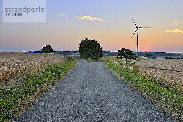 Landschaft mit Gabelstraße und Windkraftanlage in der Abenddämmerung  Bad Mergentheim  Baden-Württemberg  Deutschland