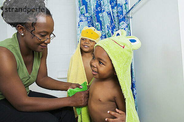 Mutter hilft Jungen beim Anziehen von Kapuzenhandtüchern nach dem Bad