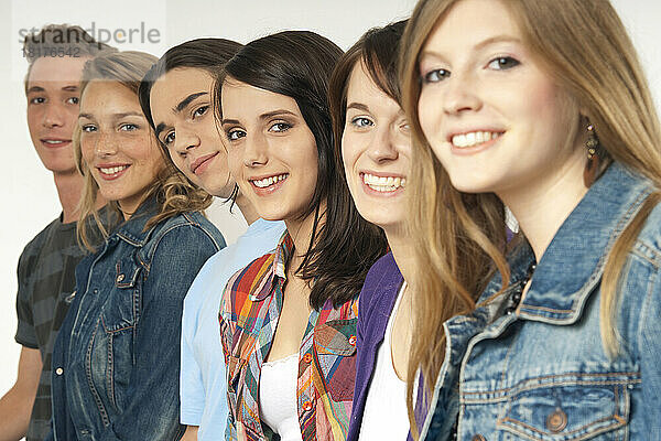 Nahaufnahmeporträt von sechs jungen Männern und jungen Frauen in einer Reihe  die lächeln und in die Kamera schauen  Studioaufnahme auf weißem Hintergrund