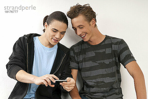 Zwei junge Männer  Freunde  die gemeinsam auf ihr Handy schauen  Studioaufnahme auf weißem Hintergrund