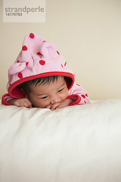 Porträt eines zwei Wochen alten  neugeborenen asiatischen Mädchens in rosa gepunkteter Kapuzenjacke  Studioaufnahme auf weißem Hintergrund