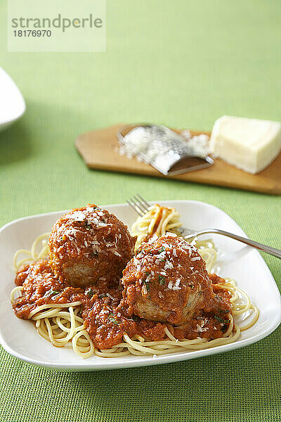 Spaghetti und Fleischbällchen mit Parmesankäse in roter Tomatensauce auf einem weißen Teller mit grüner Leinentischdecke