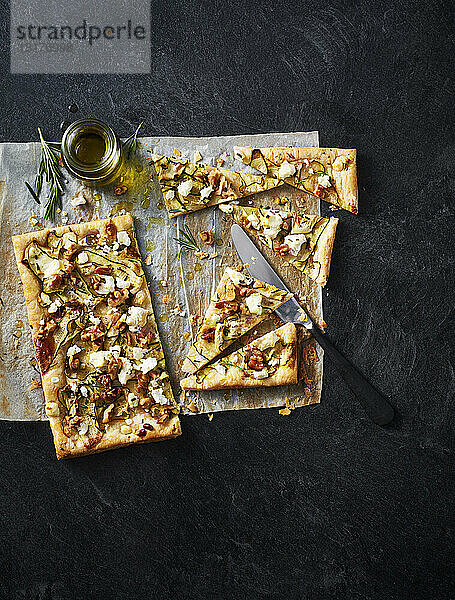 Zucchini-  Ziegenkäse- und Walnuss-Tarte auf Pergamentpapier auf schwarzem Hintergrund