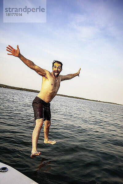 Mann springt mit glücklichem Gesichtsausdruck von einem Boot in den See  Lac Ste. Anne; Alberta Beach  Alberta  Kanada