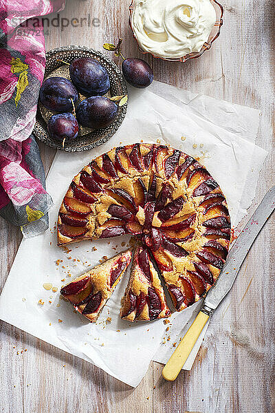 Pflaumenkuchen mit frischen Pflaumen und Schlagsahne mit herausgenommenem Stück und Serviermesser