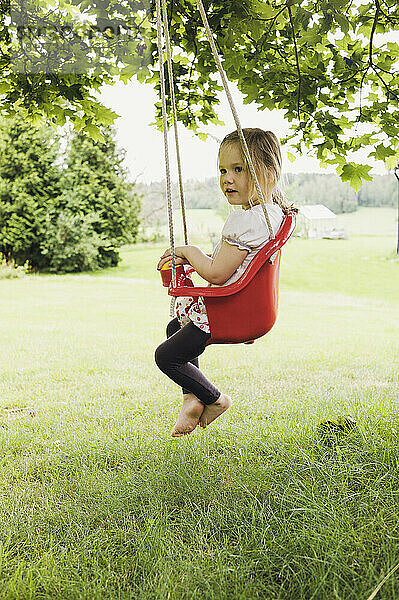 3 Jahre altes Mädchen sitzt in roter Schaukel im Hinterhof  Schweden