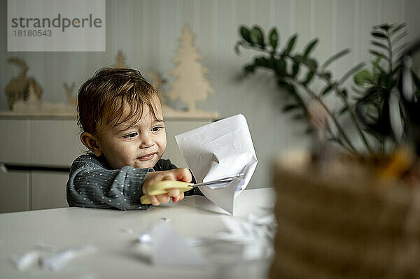 Baby boy with scissor cutting paper at table