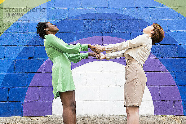 Glückliches lesbisches Paar hält Händchen vor einer bunten Wand